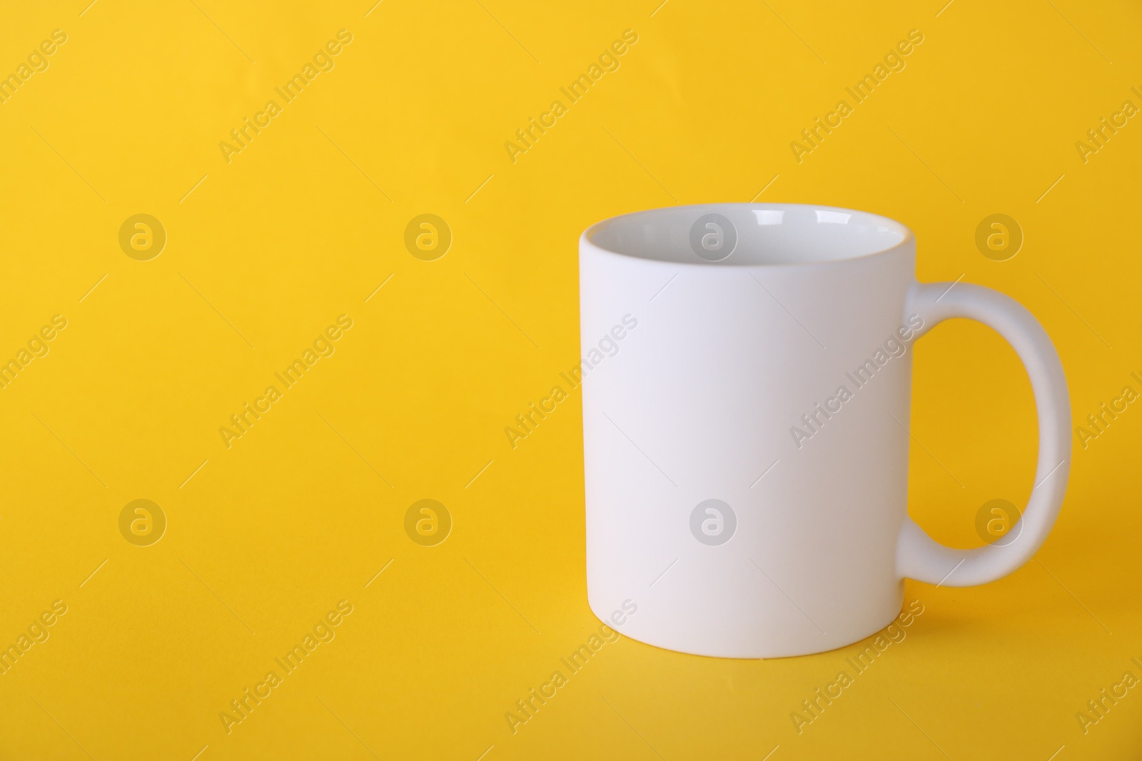 Photo of One blank white mug on yellow background. Mockup for design