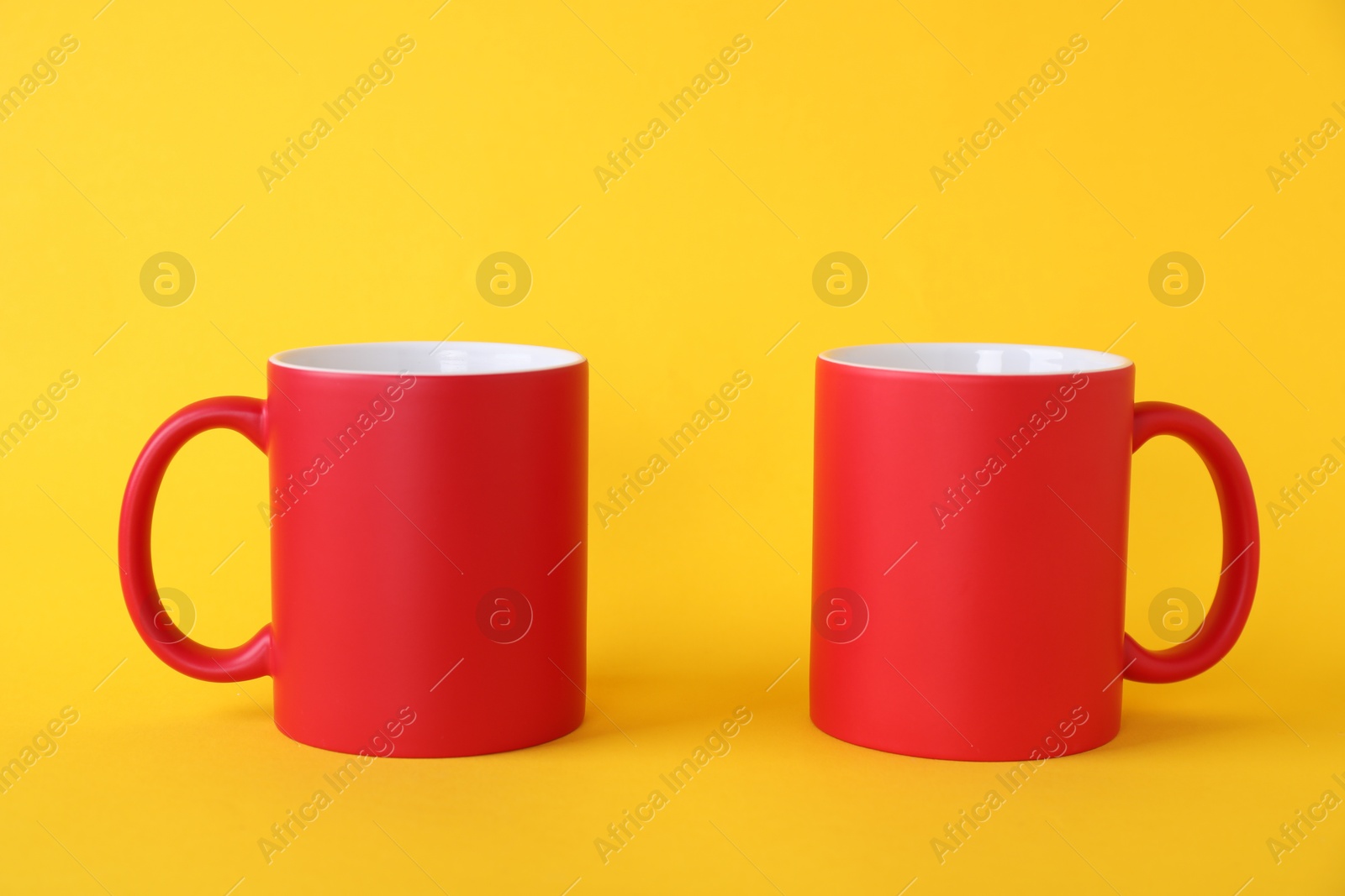 Photo of Two blank red mugs on yellow background. Mockup for design