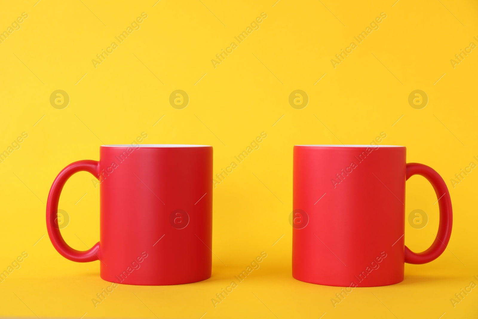 Photo of Two blank red mugs on yellow background. Mockup for design