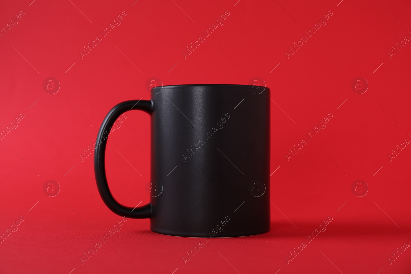 Photo of One blank black mug on red background. Mockup for design