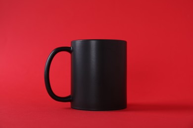 Photo of One blank black mug on red background. Mockup for design