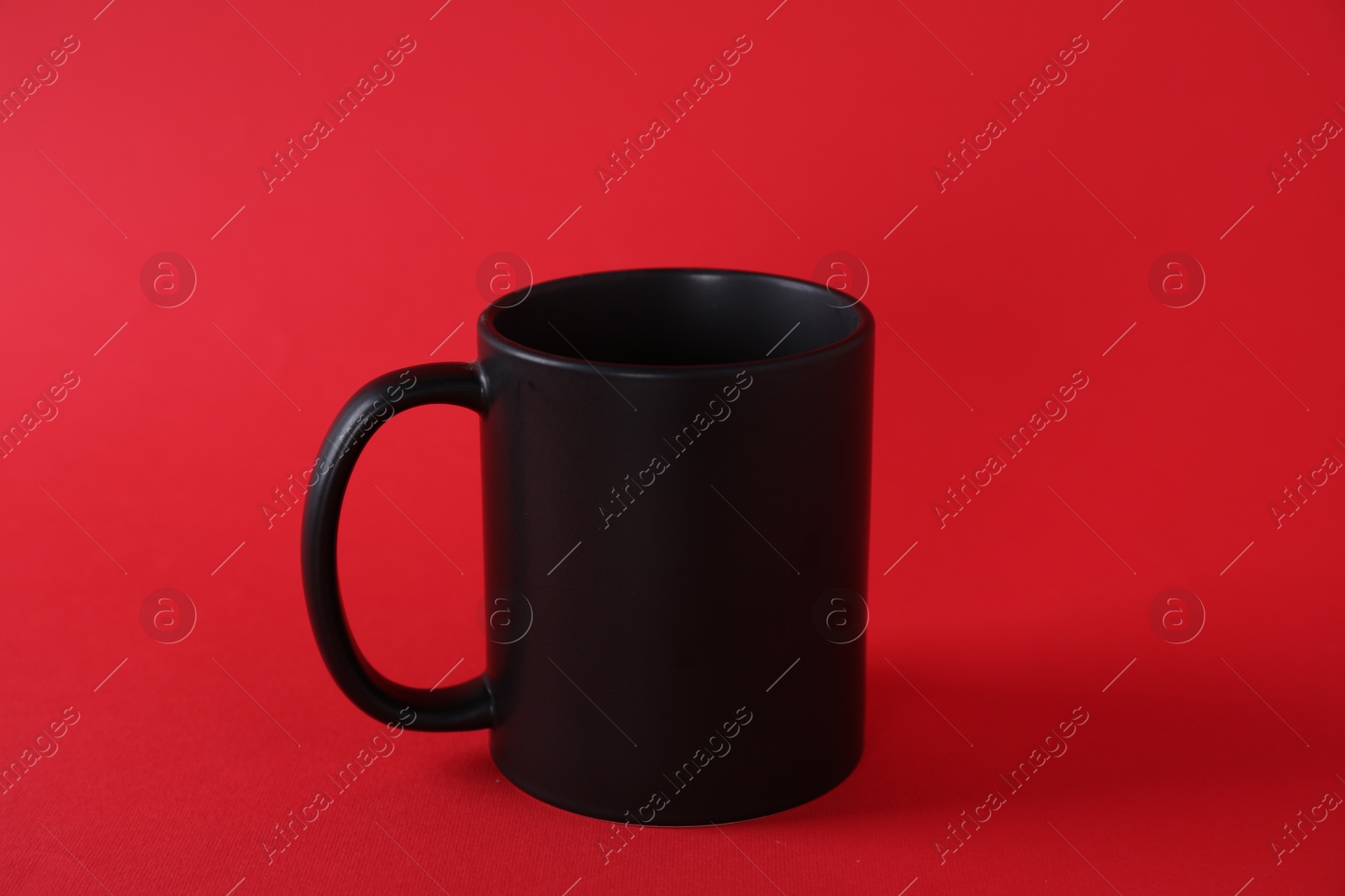 Photo of One blank black mug on red background. Mockup for design