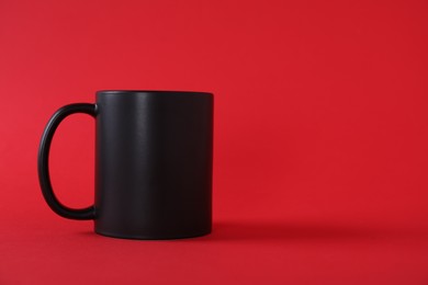 Photo of One blank black mug on red background. Mockup for design