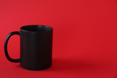 Photo of One blank black mug on red background. Mockup for design