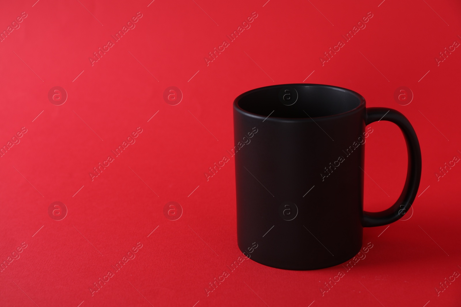 Photo of One blank black mug on red background. Mockup for design