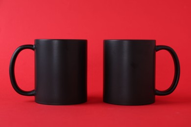 Photo of Two blank black mugs on red background. Mockup for design