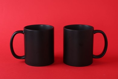 Photo of Two blank black mugs on red background. Mockup for design