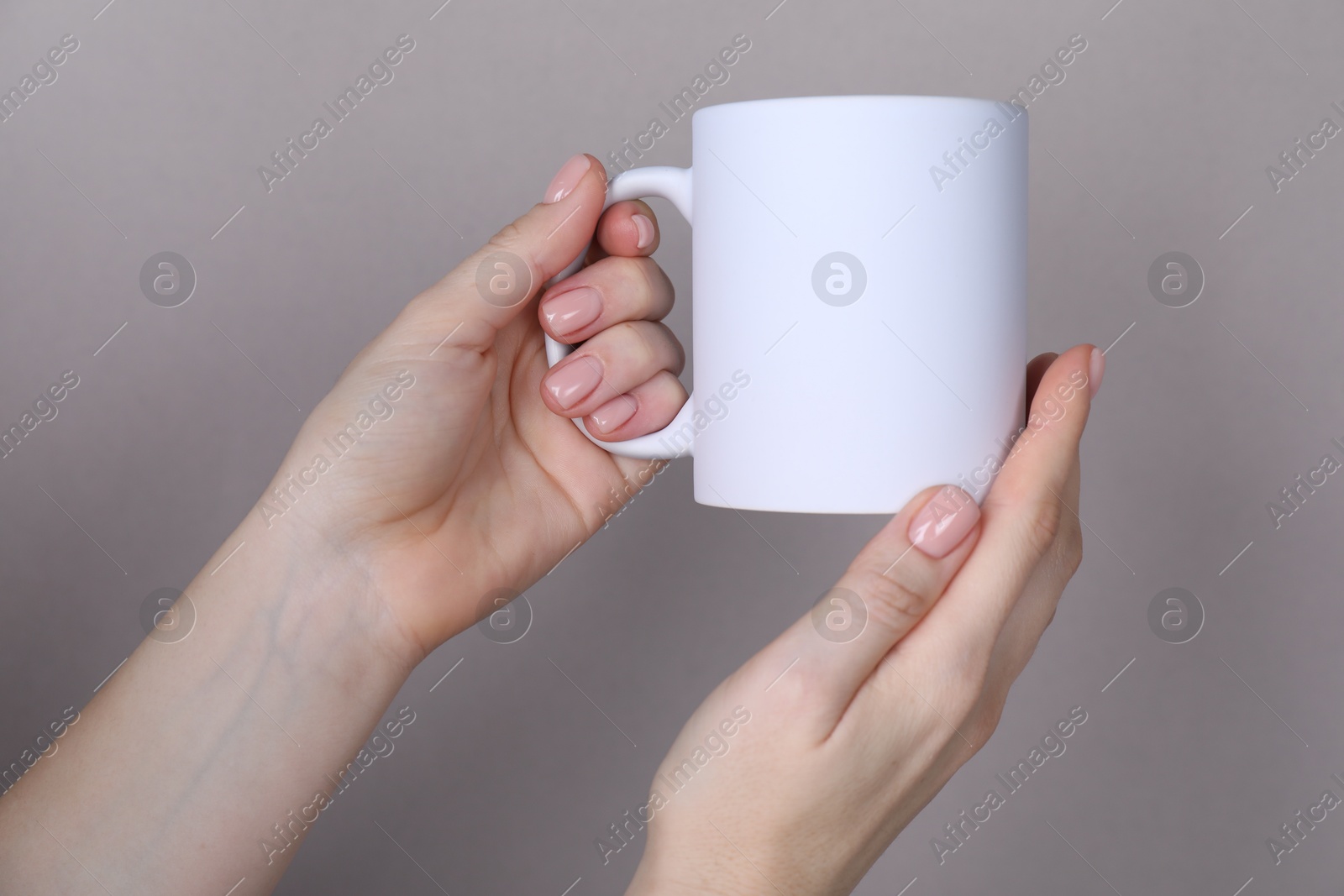 Photo of Woman holding blank white mug on grey background, closeup. Mockup for design