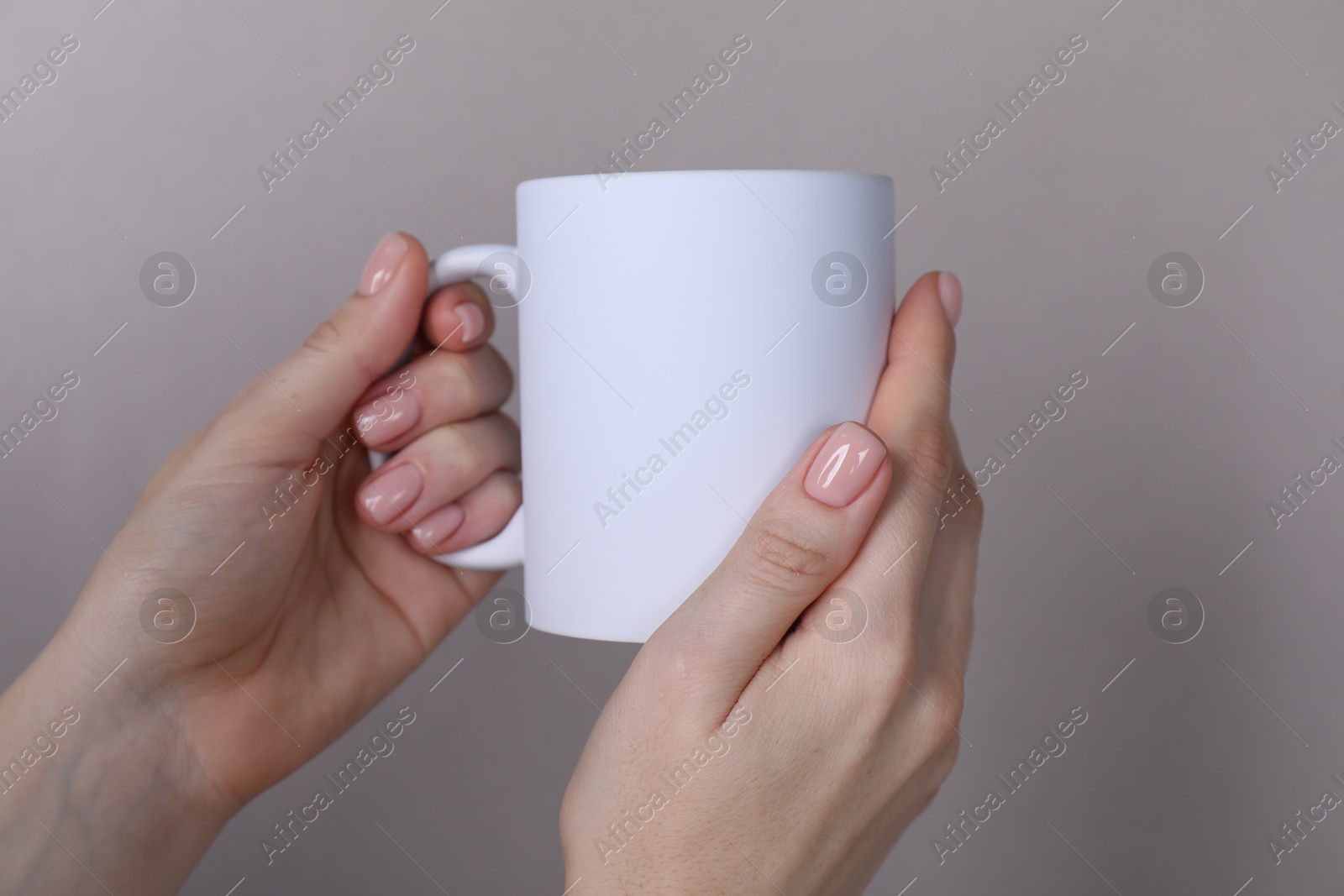 Photo of Woman holding blank white mug on grey background, closeup. Mockup for design