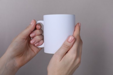 Photo of Woman holding blank white mug on grey background, closeup. Mockup for design