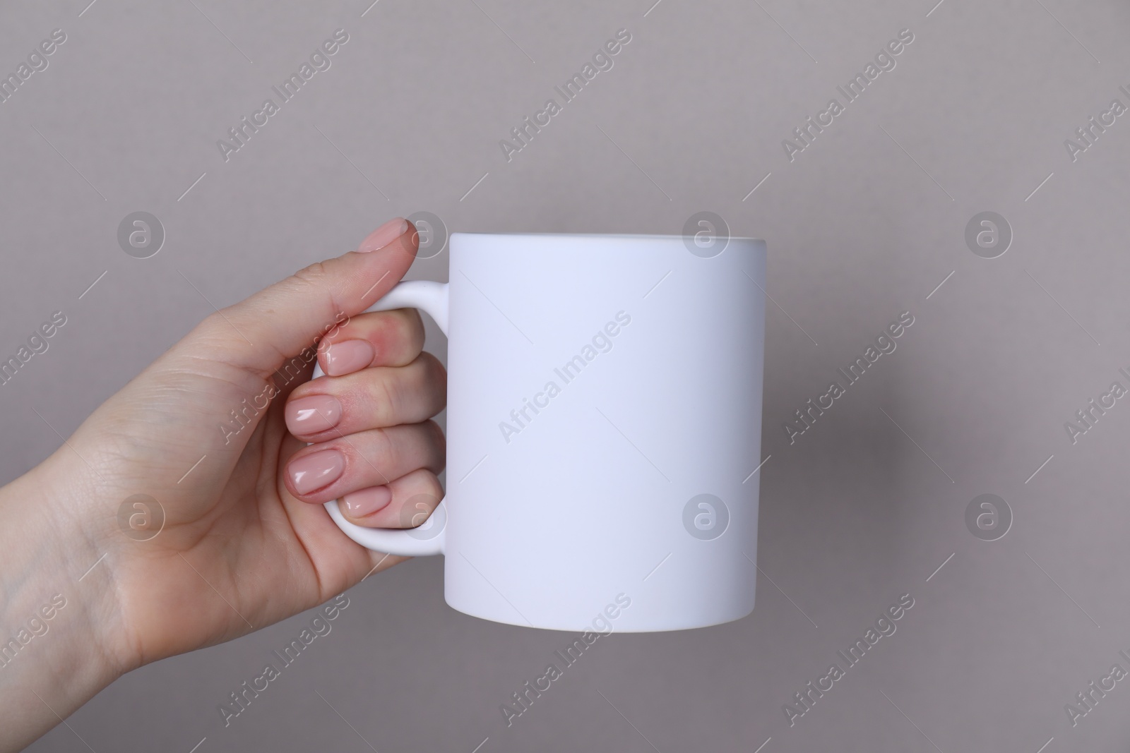 Photo of Woman holding blank white mug on grey background, closeup. Mockup for design