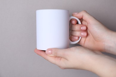 Photo of Woman holding blank white mug on grey background, closeup. Mockup for design