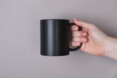 Photo of Woman holding blank black mug on grey background, closeup. Mockup for design