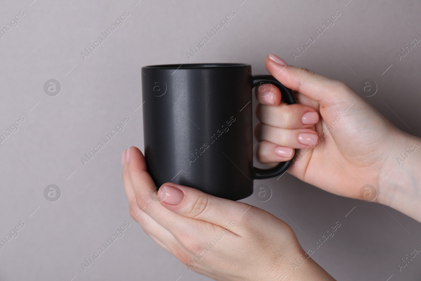 Photo of Woman holding blank black mug on grey background, closeup. Mockup for design