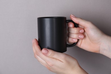 Photo of Woman holding blank black mug on grey background, closeup. Mockup for design