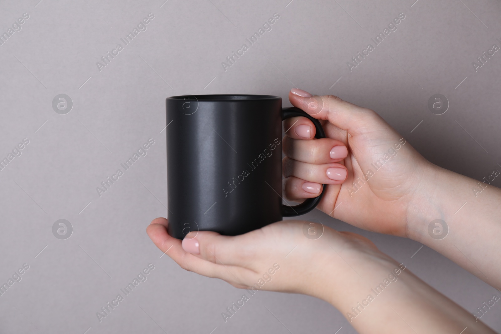 Photo of Woman holding blank black mug on grey background, closeup. Mockup for design