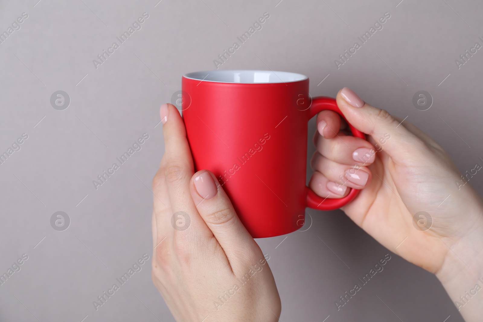 Photo of Woman holding blank red mug on grey background, closeup. Mockup for design