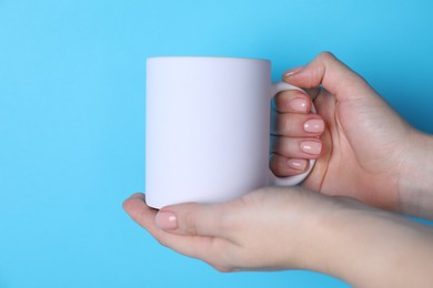 Photo of Woman holding blank white mug on light blue background, closeup. Mockup for design