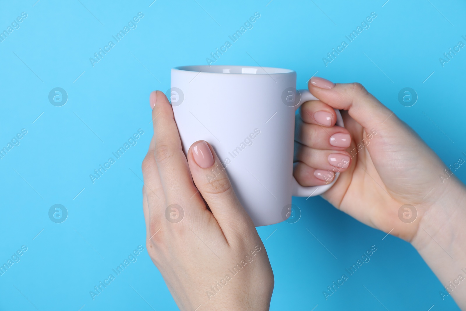 Photo of Woman holding blank white mug on light blue background, closeup. Mockup for design