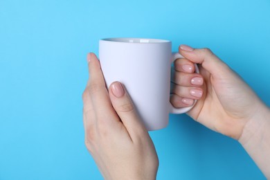 Photo of Woman holding blank white mug on light blue background, closeup. Mockup for design