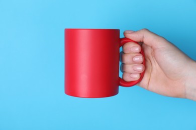 Photo of Woman holding blank red mug on light blue background, closeup. Mockup for design