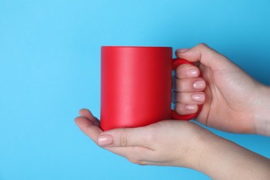 Photo of Woman holding blank red mug on light blue background, closeup. Mockup for design