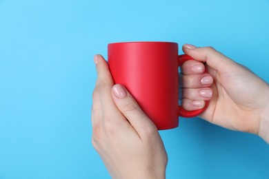 Photo of Woman holding blank red mug on light blue background, closeup. Mockup for design