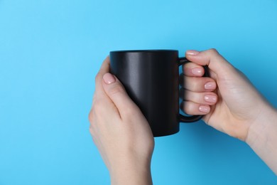 Photo of Woman holding blank black mug on light blue background, closeup. Mockup for design