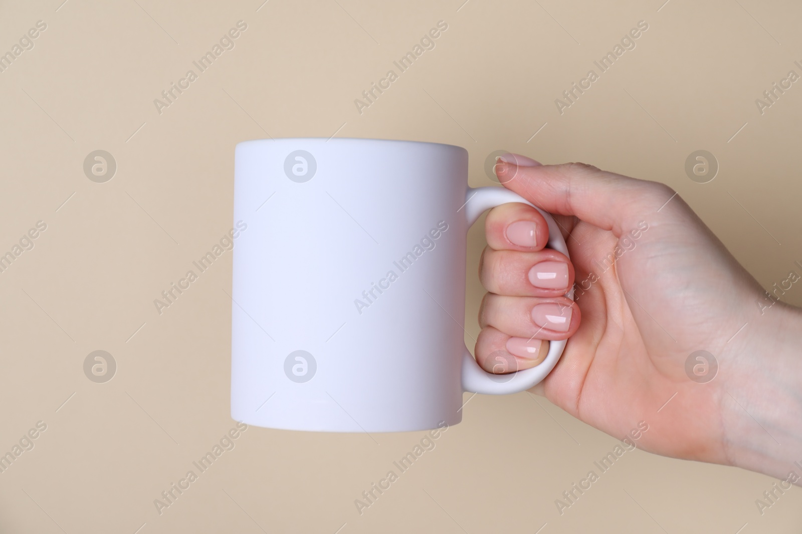 Photo of Woman holding blank white mug on beige background, closeup. Mockup for design