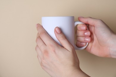 Photo of Woman holding blank white mug on beige background, closeup. Mockup for design