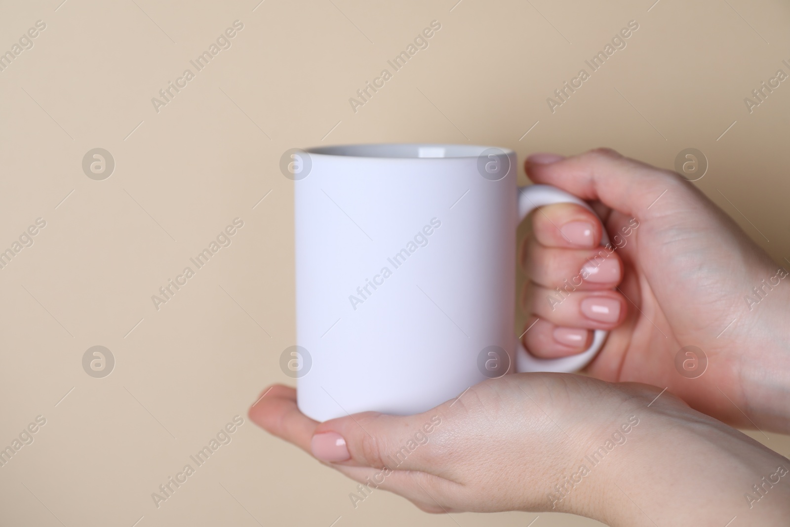 Photo of Woman holding blank white mug on beige background, closeup. Mockup for design