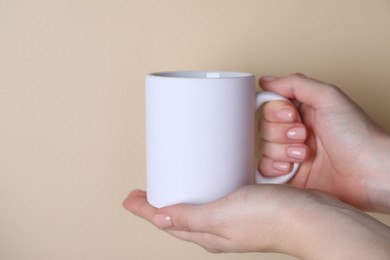 Photo of Woman holding blank white mug on beige background, closeup. Mockup for design