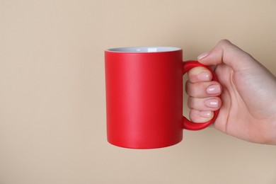 Photo of Woman holding blank red mug on beige background, closeup. Mockup for design