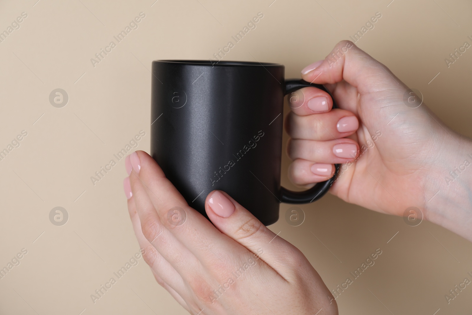 Photo of Woman holding blank black mug on beige background, closeup. Mockup for design