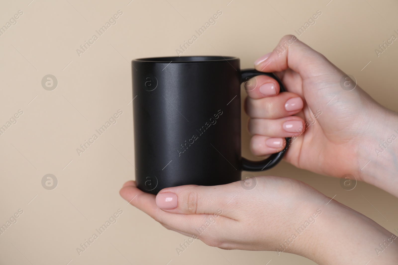 Photo of Woman holding blank black mug on beige background, closeup. Mockup for design