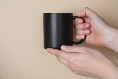 Photo of Woman holding blank black mug on beige background, closeup. Mockup for design