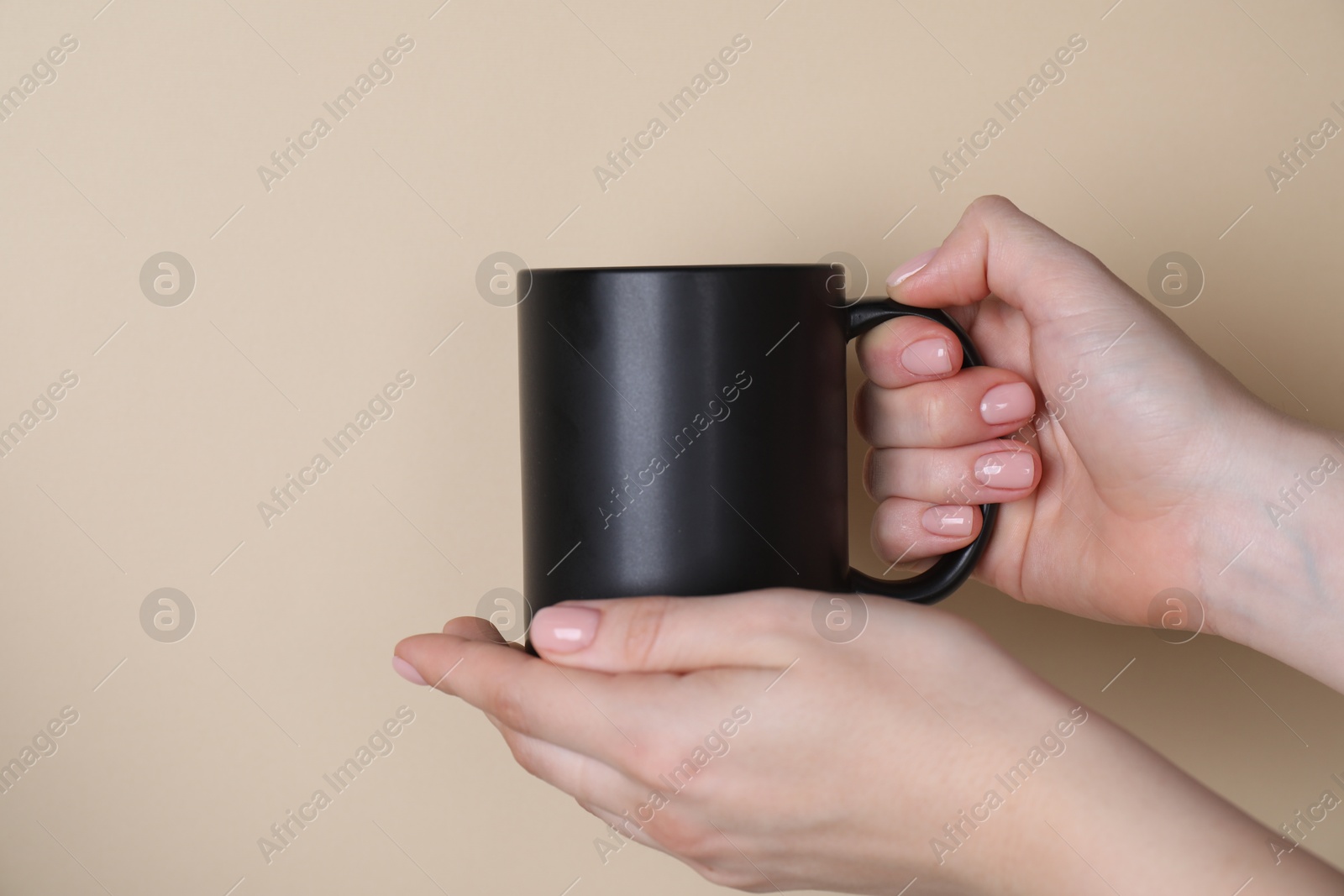 Photo of Woman holding blank black mug on beige background, closeup. Mockup for design