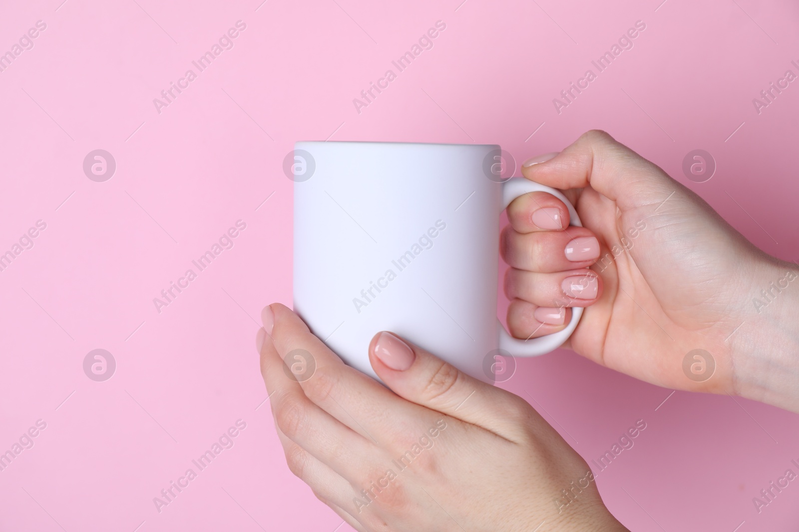 Photo of Woman holding blank white mug on pink background, closeup. Mockup for design