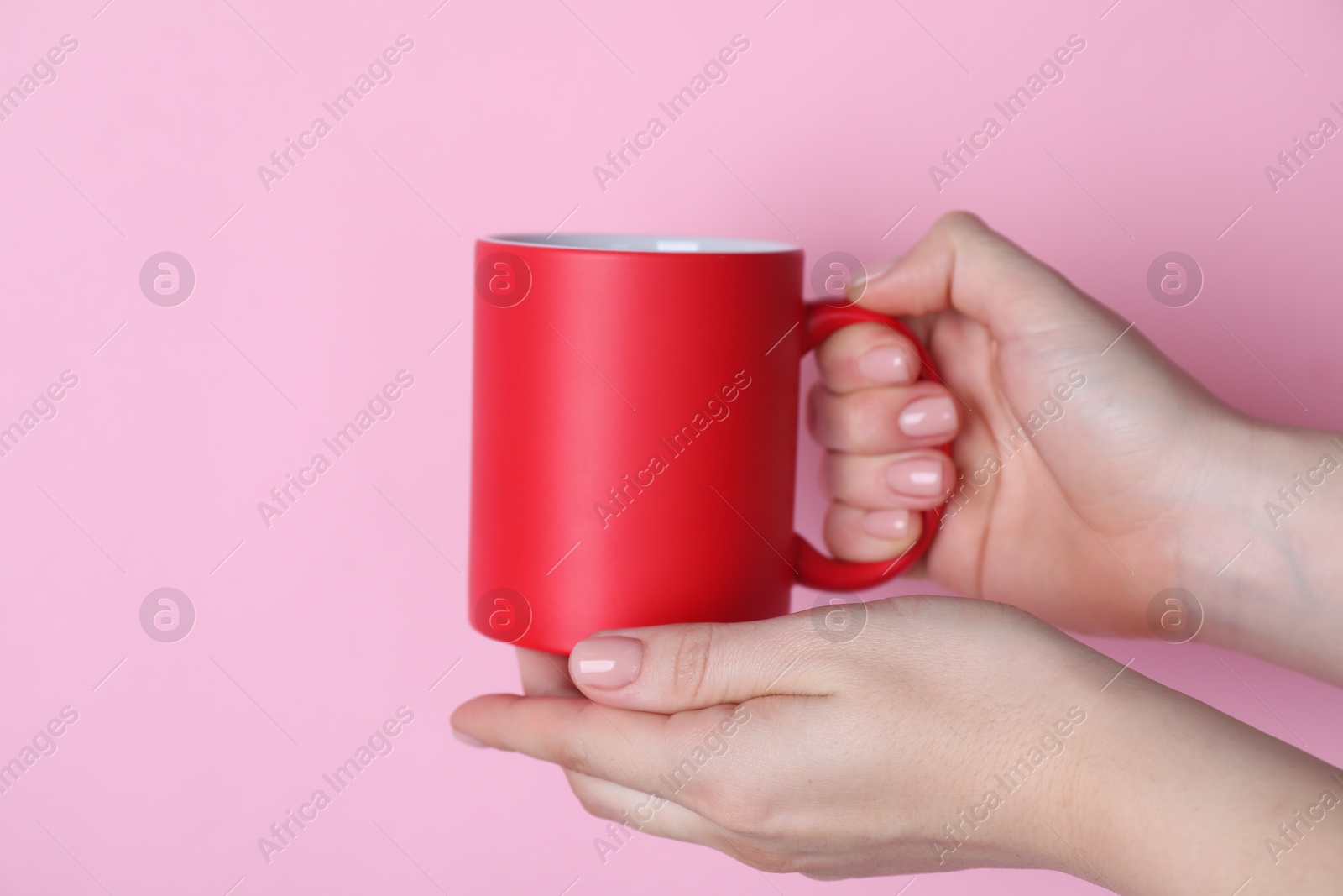 Photo of Woman holding blank red mug on pink background, closeup. Mockup for design