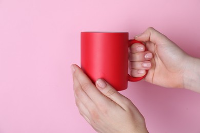 Photo of Woman holding blank red mug on pink background, closeup. Mockup for design