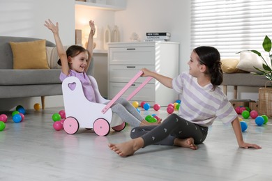 Photo of Cute little sisters playing with wooden stroller at home