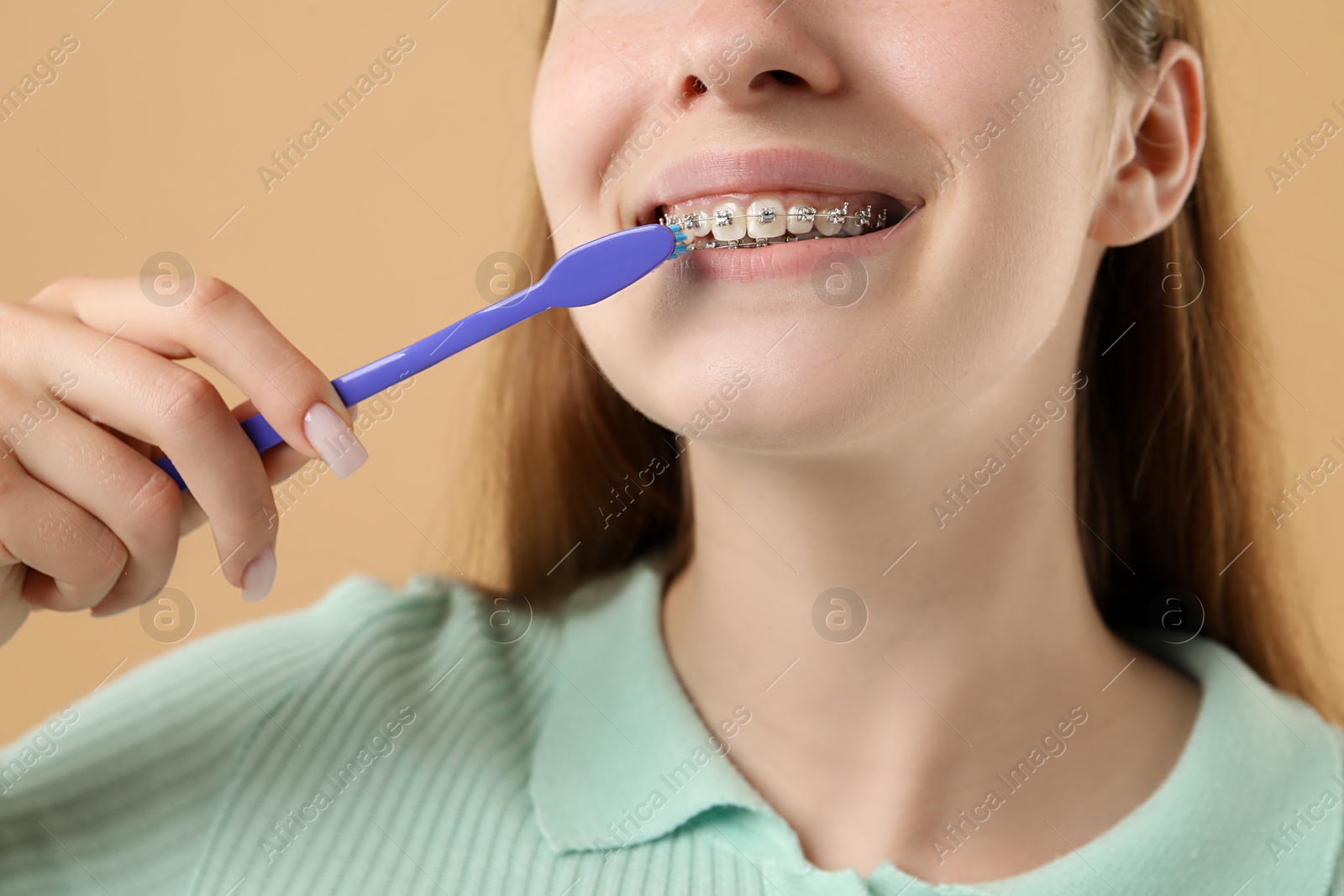 Photo of Girl with braces cleaning teeth on beige background, closeup