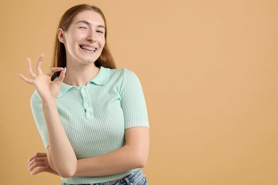 Photo of Smiling girl with braces showing ok gesture on beige background, space for text