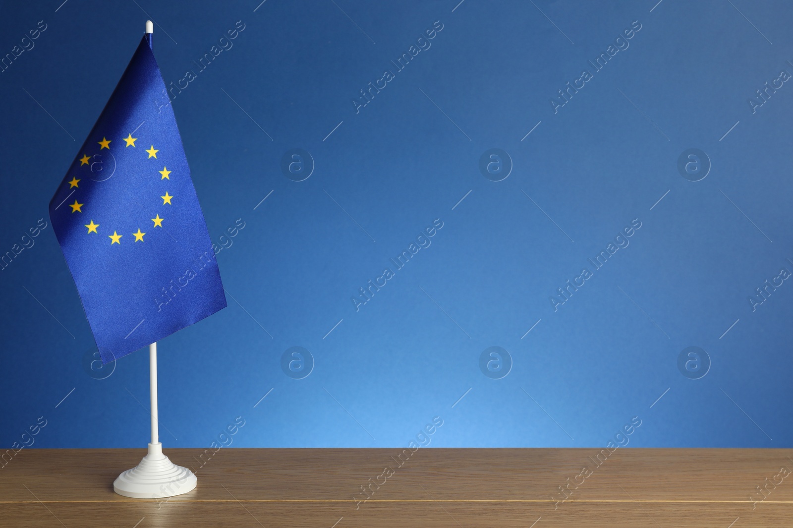 Photo of One flag of European Union on wooden table against blue background. Space for text