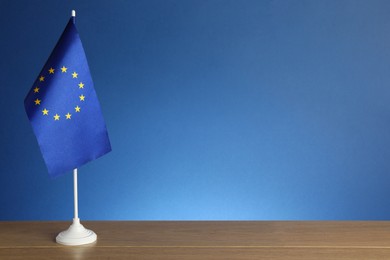 Photo of One flag of European Union on wooden table against blue background. Space for text