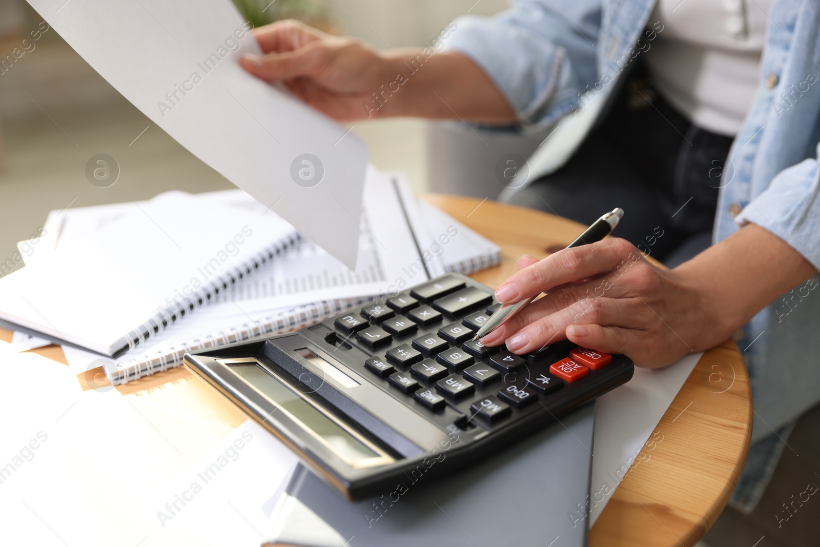 Photo of Budget planning. Woman using calculator while working with accounting document at table indoors, closeup