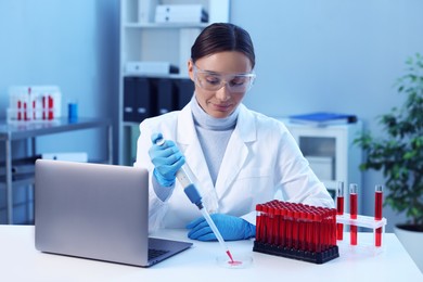 Laboratory testing. Doctor dripping blood sample into Petri dish at table indoors