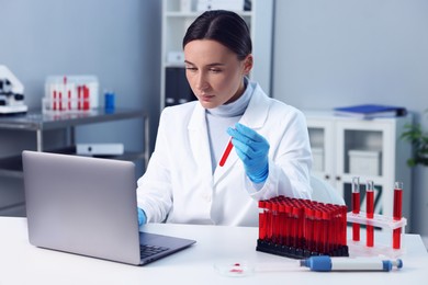 Photo of Laboratory testing. Doctor holding test tube with blood sample at table indoors