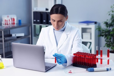 Photo of Laboratory testing. Doctor holding test tube with blood sample at table indoors