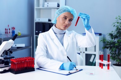 Photo of Laboratory testing. Doctor with blood sample taking notes at table indoors